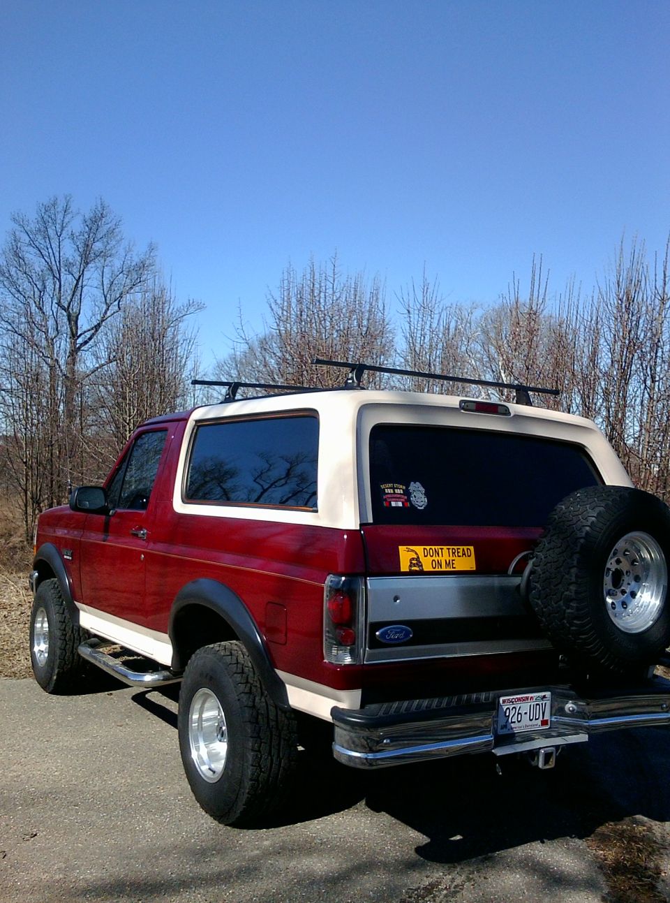 Red and tan Ford Bronco parked on a road with trees in the background. It has a spare tire mounted on the back and a 'Don't Tread On Me' sticker