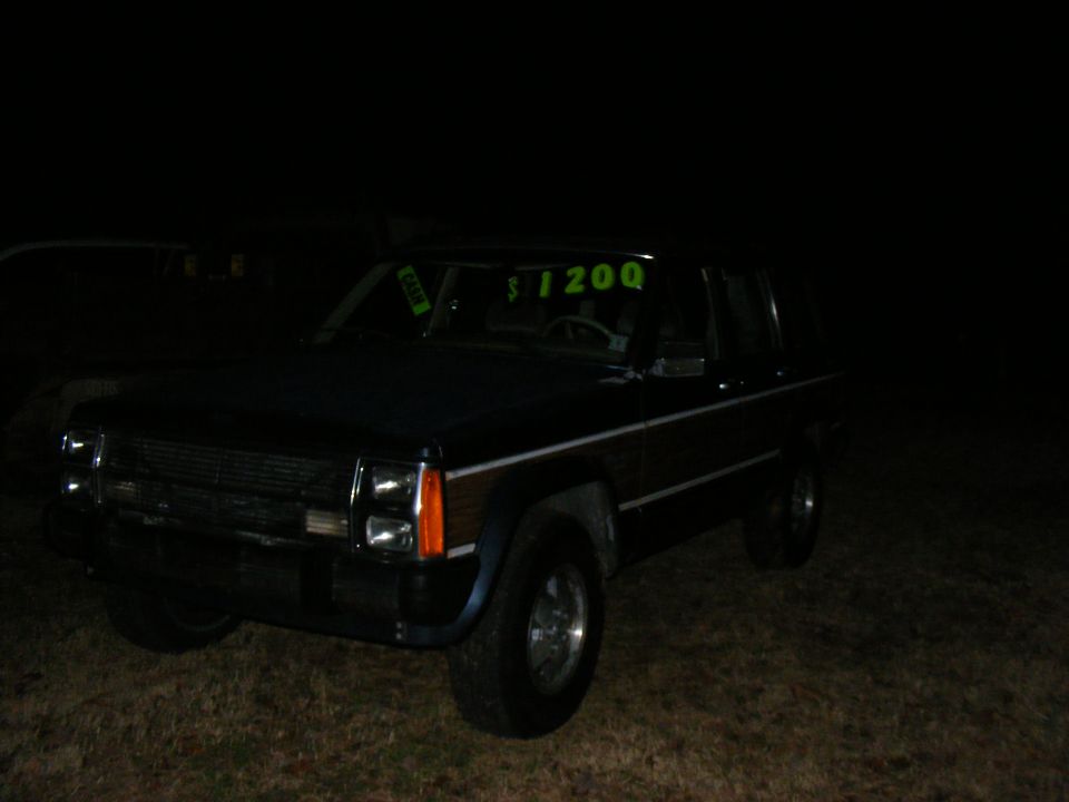 dark SUV with wood paneling and a '$1200' sign in the windshield, parked at night