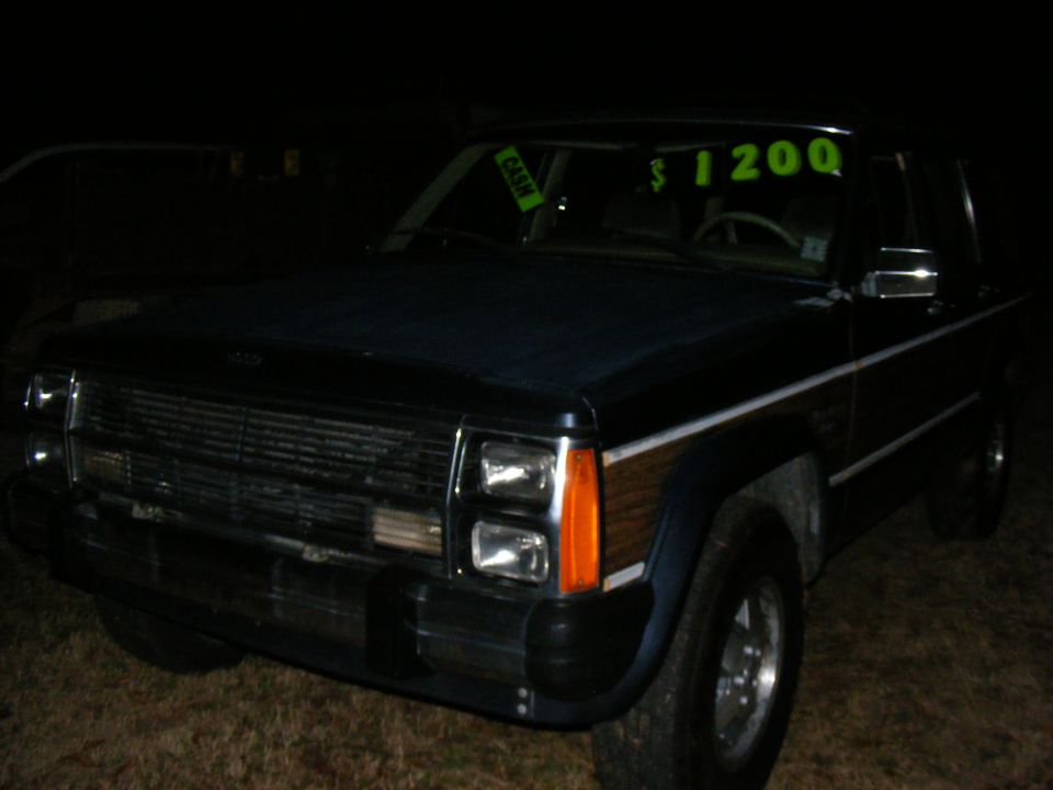 Dark blue Jeep Cherokee Wagoneer with wood paneling. Price tag in window says $1200