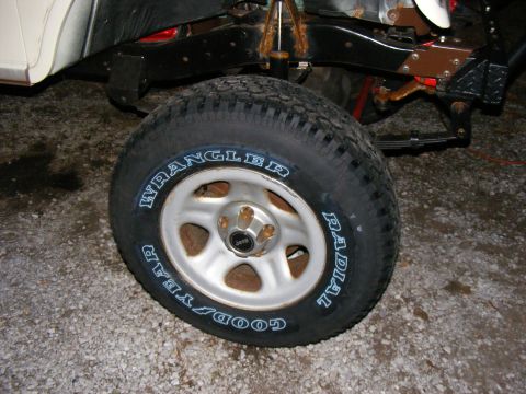 Tire with 'Goodyear Wrangler Radial' text on a silver wheel, showing part of the vehicle's black frame and whi