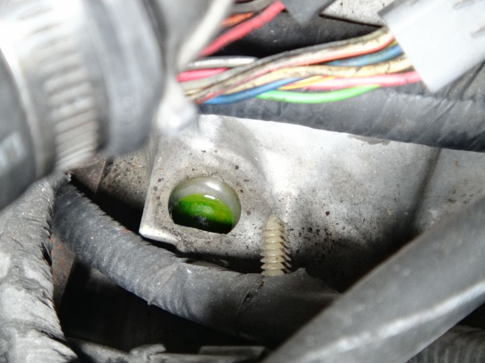 Close-up of green engine coolant leaking from a small opening in metal engine component, with wires in background