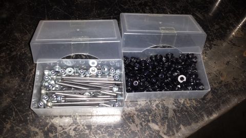 1996 Ford Bronco - Two containers of assorted hardware, including bolts, nuts, and washers, are organized on a dark surface.