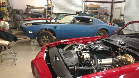 1970 Pontiac Trans Am - Multiple Pontiac Firebirds are in a garage, with one red car's engine prominently displayed.