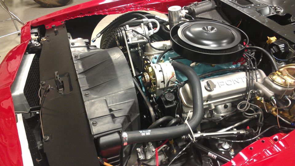 Pontiac V8 engine bay with air cleaner, alternator, and radiator visible. 'PONTIAC' stamped on valve cover