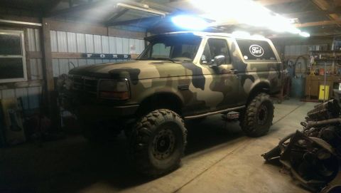 1995 Ford Bronco - This Ford Bronco is parked inside a garage and features a camouflage paint job and oversized tires.