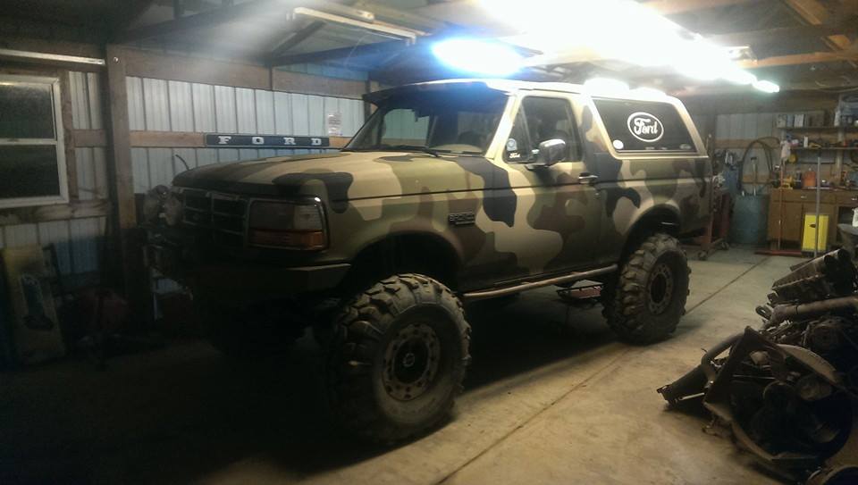 Camouflaged Ford Bronco parked in a garage with large tires