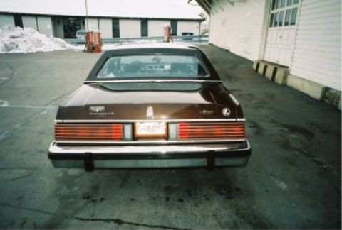 1984 Mercury Grand Marquis - The rear of a brown sedan is visible, with a license plate and "SUPERMOTORS" watermark.