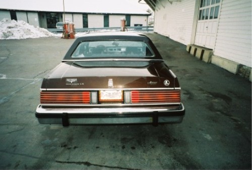 Rear view of a brown Mercury sedan with full-width taillights on wet pavement