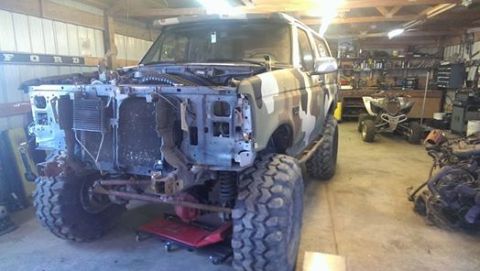 1995 Ford Bronco - A Ford Bronco in a garage, missing its front grille and bumper, with camouflage paint.