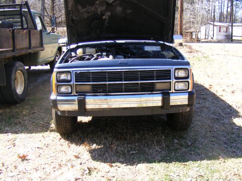 Jeep Cherokee front with hood open, chrome bumper, and grille. Another truck is partially visible to the left