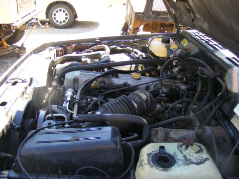 Engine bay of a Jeep Cherokee, with another vehicle visible in the background