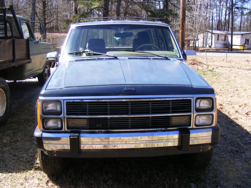 Jeep Cherokee front view, light blue with black hood, chrome bumper, parked outdoors