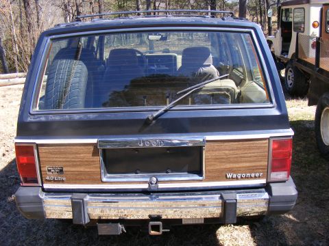 Jeep Wagoneer rear with wood paneling and spare tire inside. Another vehicle is partially visible to the right