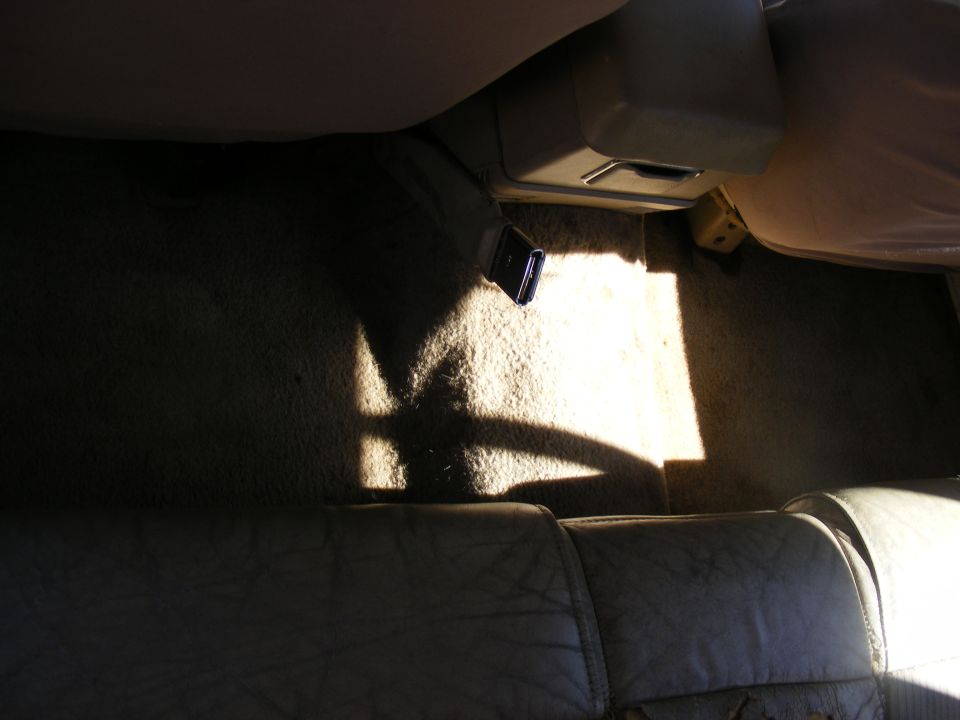 Interior view of vehicle floor with sunlight casting shadows, showing carpet and part of a seat