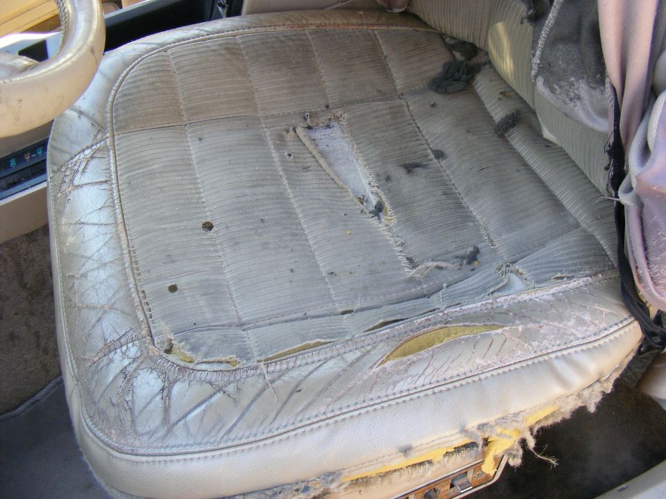 Torn white vinyl car seat with diamond stitching and exposed foam