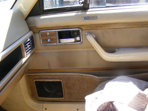 Interior door panel of a Jeep Wagoneer, showing the door handle, speaker, and vent