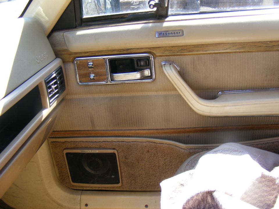 Interior door panel of a Jeep Wagoneer, showing the door handle, speaker, and vent