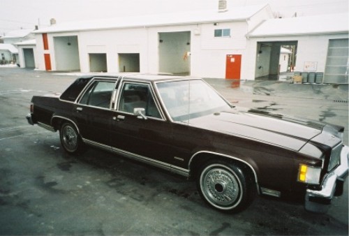 Maroon full-size four-door sedan with wire wheel covers on wet pavement