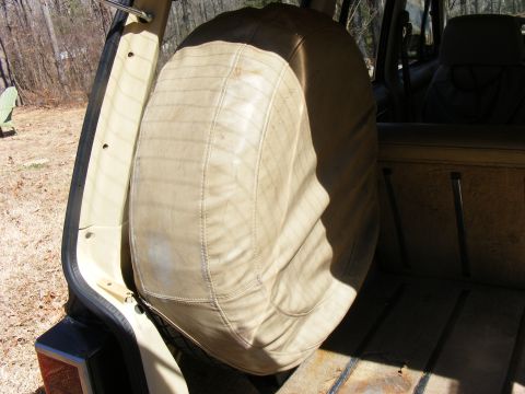 Tan vinyl spare tire cover inside the cargo area of an older SUV