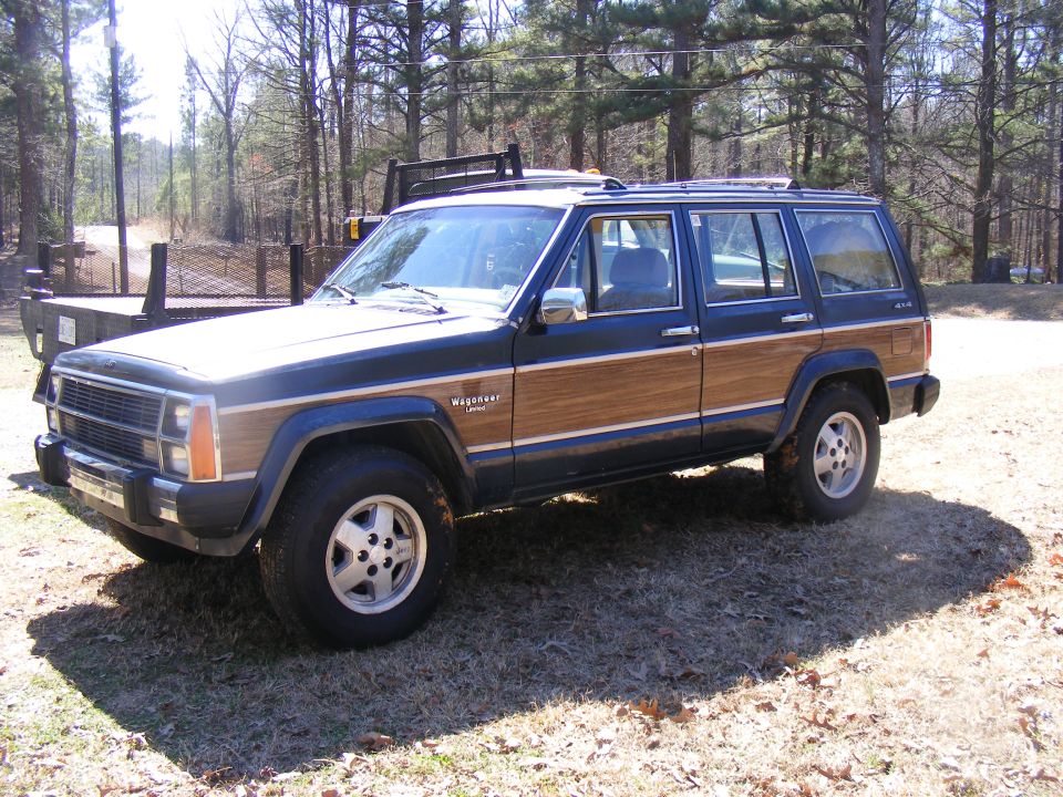 Wood-paneled Jeep Grand Wagoneer parked on grassy area with trees in background