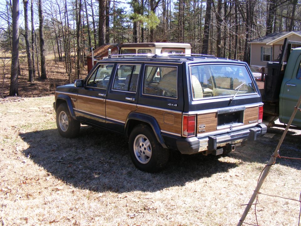 Wood-paneled Jeep Cherokee Wagoneer, rear 3/4 view, parked on dry grass