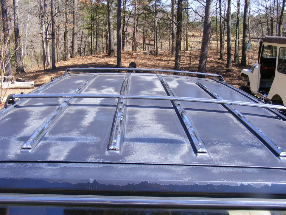 Close-up of a dark vehicle's roof rack with a light-colored vehicle in the background