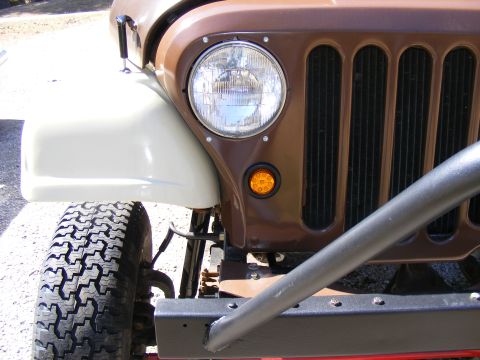 Front corner of brown Jeep CJ-5 with white fender and roll bar. Supermotors logo visible