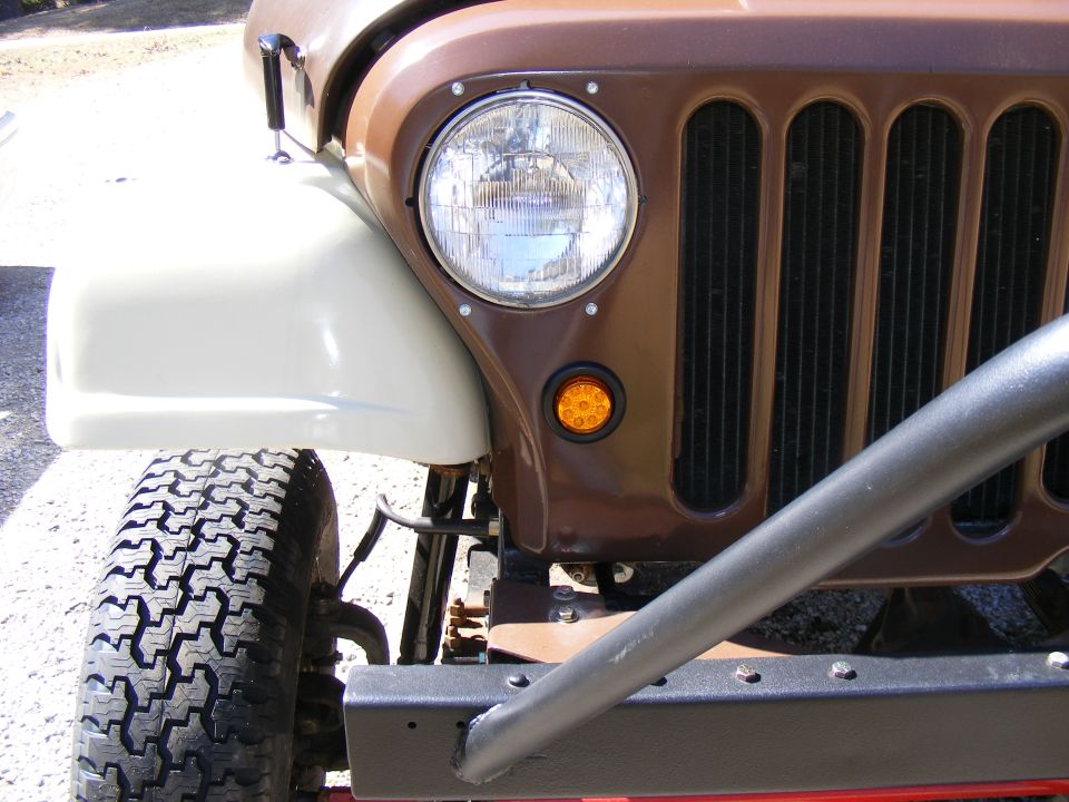 Front corner of brown Jeep CJ-5 with white fender and roll bar. Supermotors logo visible