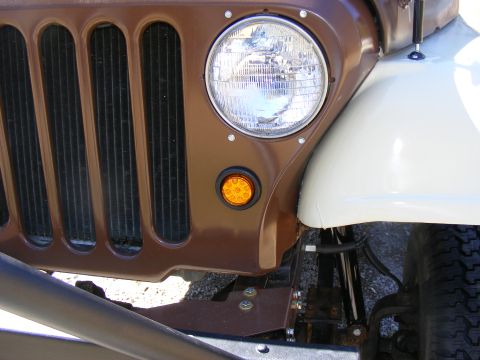 Brown Jeep CJ grille with vertical slots and a round headlight, next to a white fender