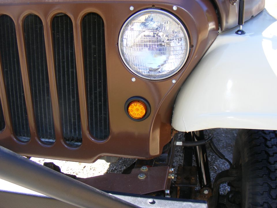 Brown Jeep CJ grille with vertical slots and a round headlight, next to a white fender