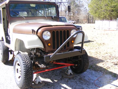 Jeep CJ-5 front end, painted brown and white, on jack stands. Another vehicle is visible behind it