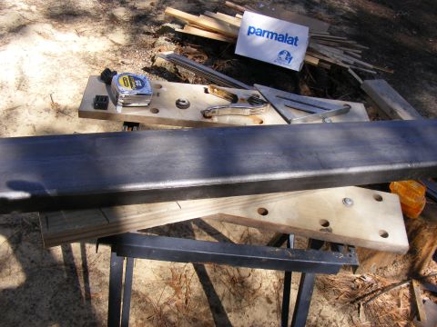 Metal bar on sawhorses with tape measure, clamps, and a Parmalat box