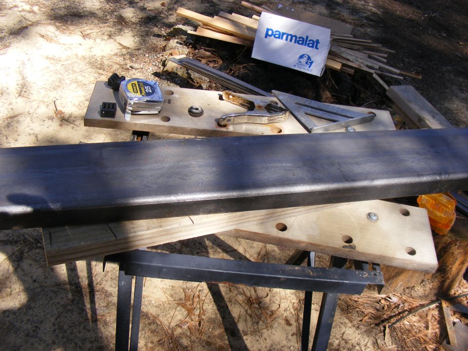 Metal bar on sawhorses with tape measure, clamps, and a Parmalat box