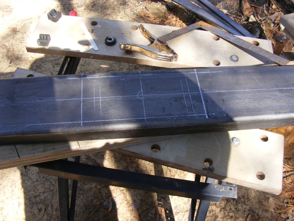 Metal beam with chalk lines and measurements, clamped to a wooden jig