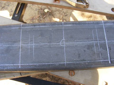 Metal beam with chalk lines and a circle drawn on it, resting on sawhorses