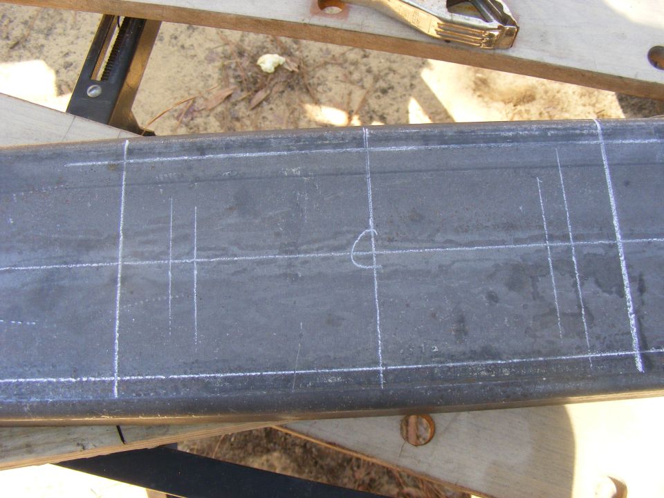 Metal beam with chalk lines and a circle drawn on it, resting on sawhorses