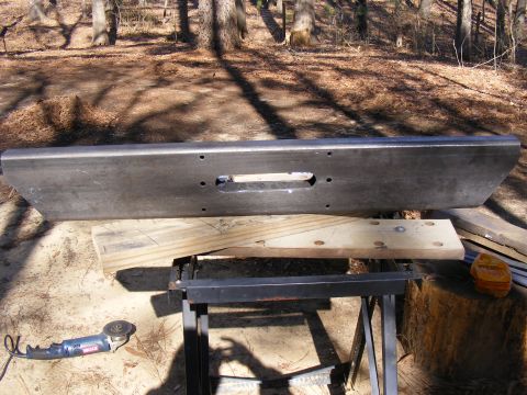 Aftermarket steel bumper with winch cutout, resting on sawhorses outdoors