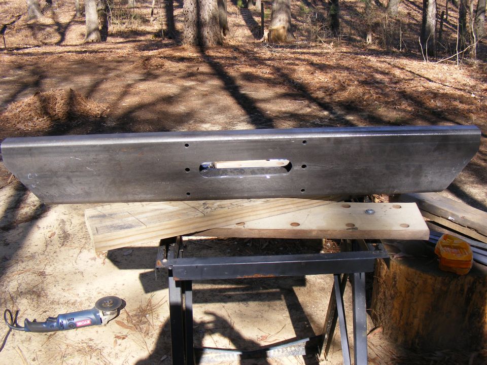 Aftermarket steel bumper with winch cutout, resting on sawhorses outdoors
