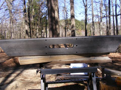Aftermarket front bumper with a winch cutout, resting on sawhorses outdoors