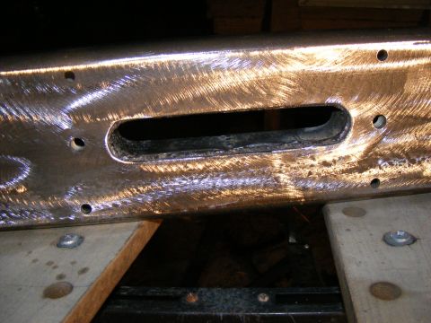 Close-up of a metal bumper, showing a rectangular cutout and several bolt holes. It's been ground and polished