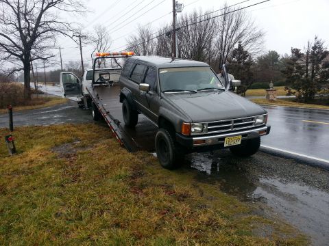 1987 Toyota 4Runner - A gray 1987 Toyota 4Runner is loaded onto a tow truck on a wet day.