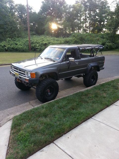1987 Toyota 4Runner - This lifted Toyota pickup truck, likely from the mid-1980s, is parked curbside with a soft top covering the bed.