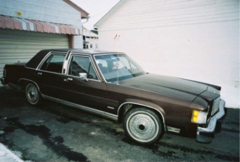 1984 Mercury Grand Marquis - A brown 1984 Mercury Grand Marquis sedan is parked in front of a garage.