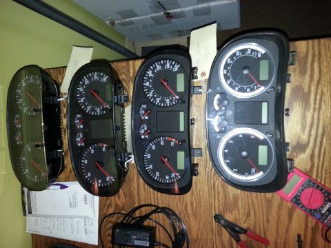 2002 Volkswagen Jetta - Several Volkswagen instrument clusters are displayed on a wooden surface, with one cluster connected to a multimeter.
