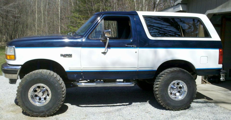 Side view of a lifted 1994 Ford Bronco with two-tone blue and white paint and large off-road tires