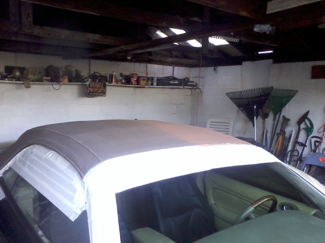 Car interior with convertible top covered in tape, parked in a garage with tools on the wall