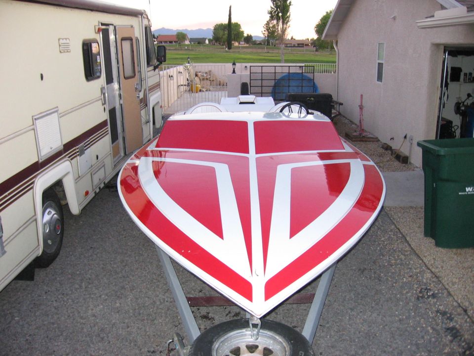 Red and white speedboat on trailer parked beside RV in driveway