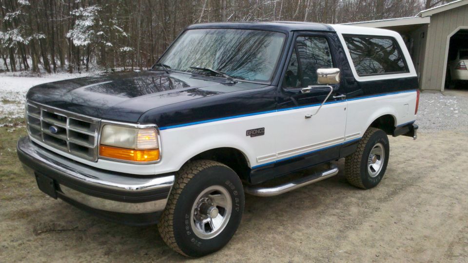 Two-tone blue and white Ford Bronco parked outside in a wooded area
