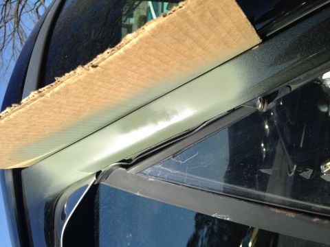 1990 Ford Bronco - Close-up of a black vehicle's window frame, partially covered by a piece of cardboard.