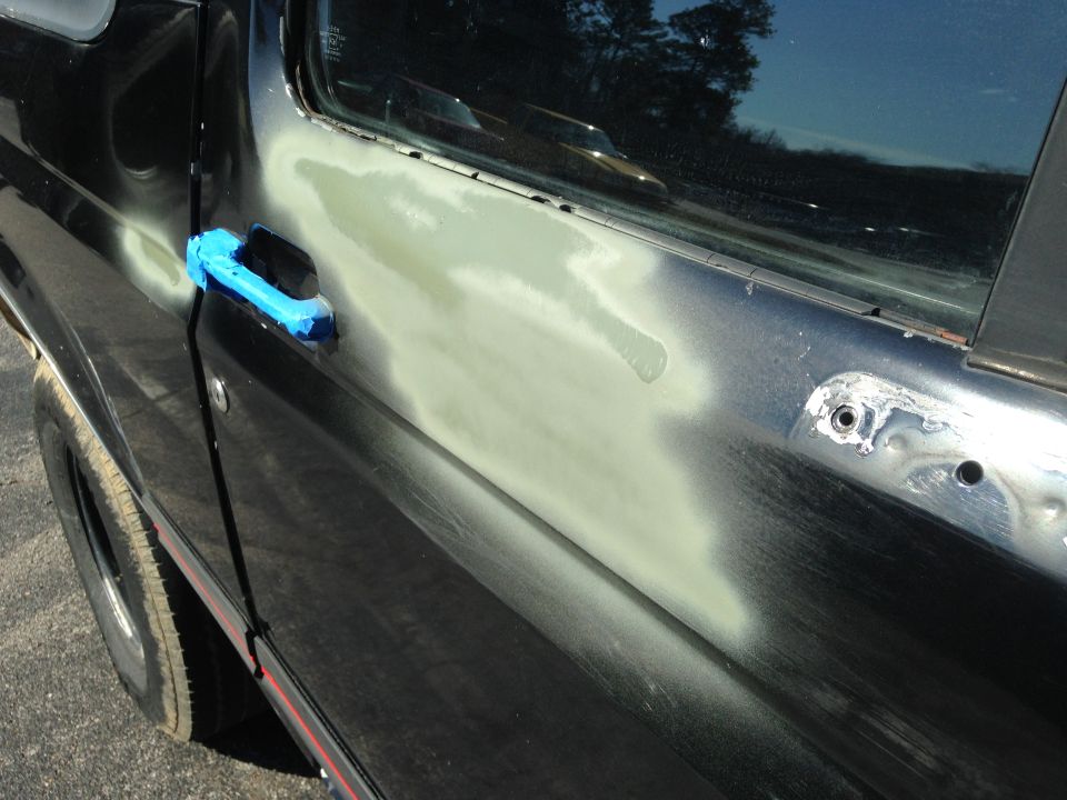 1990 Ford Bronco door with body filler applied to the panel and blue tape on the handle
